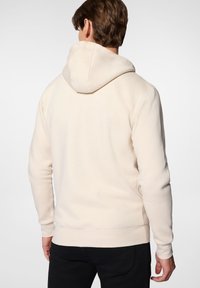 Beżowa bluza z kapturem o gładkiej teksturze, z prążkowanymi mankietami i dołem. Posiada regulowany kaptur oraz prosty, minimalistyczny design.