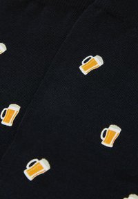 Tela oscura con pequeños iconos impresos de jarra de cerveza llenos de líquido ámbar y espuma blanca, dispersos por la superficie.