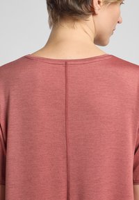 Kurzärmliges, rosefarbenes Oberteil aus einem strukturierten Stoff. Verfügt über einen runden Halsausschnitt und eine sichtbare Naht auf der Rückseite.