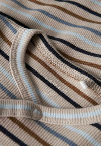 Pasiasty ubranie o ribbowanej teksturze w odcieniu beżowym, z niebieskimi, brązowymi i granatowymi paskami. Posiada okrągły dekolt i detal z guzikami.