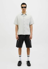 Camisa de botones de manga corta en verde claro con un bolsillo en el pecho, combinada con pantalones cortos de mezclilla oscura, calcetines a rayas blancos y zapatos negros.