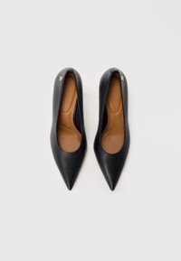 Sorte læder højhælede sko med spidse tæer og glat tekstur. Har en tan sål og en lille metallisk logoaccent nær hælen.