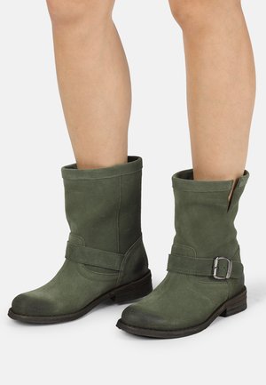 Stivali alla caviglia in suede verde con risvolto, tacco piatto, zip laterale e una fascia decorativa con dettaglio della fibbia in argento.