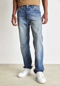 Blå denimjeans med en lätt blekt finish, rak bendesign, femficksstil och klassisk metallknappstängning i midjan.
