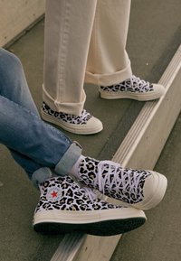 Zapatillas altas con un fondo blanco y un diseño de estampado de leopardo en negro y marrón. Suela de goma y cordones blancos.