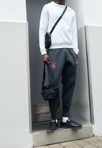 Grijze sweatpants met roze details, witte crewneck sweatshirt, zwarte sneakers en een kleine zwarte crossbody tas. Eenvoudig ontwerp en casual look.