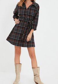 Kostkovaná šatová šaty v tmavých odstínech, s límečkem, dlouhými rukávy a páskem na zavázání v pase. Spárované s béžovými kozačkami po kolena.