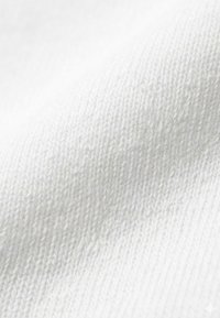 Gros plan sur un tissu tricoté blanc montrant la texture détaillée et le motif de tissage.