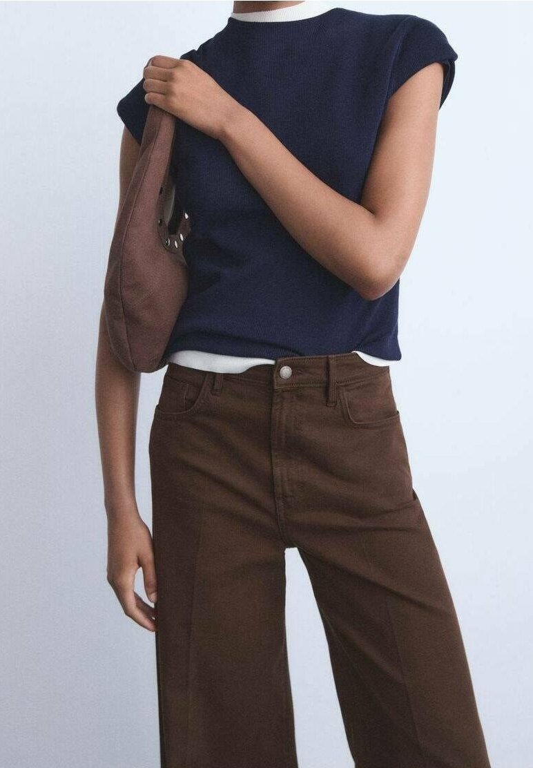 Personne portant un haut sans manches bleu marine, un pantalon marron taille haute et portant un sac marron sur une épaule.