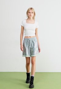 Light gray athletic shorts with green accents and drawstring, paired with a fitted white crop top and black combat boots. Smooth texture.