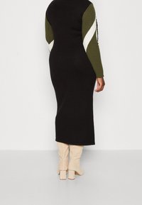 Abito a maglia nero con maniche a righe verdi e bianche, silhouette aderente, lunghezza midi, abbinato a stivali al ginocchio beige con tacco a blocco.