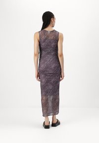 Μακριφόρεμα σε μωβ απόχρωση με διαφανή επικάλυψη και κυματιστό σχέδιο. Διαθέτει ραφή με πτυχές και ευθεία κάτω άκρη. Συνδυάζεται με χοντρά μαύρα υποδήματα.