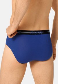 Blaue Baumwollslips mit einem schwarzen Bund, der ein blaues Textlogo trägt, mit glatter Textur und passgenauer Form von hinten betrachtet.