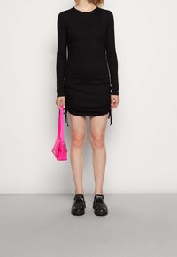 Svart långärmad klänning med sidofåll, rosa handväska och svarta sandaler med grova sulor. Slät struktur och figursydd design.