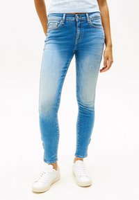 Jeans ajustados de color azul claro con un lavado desgastado, con una cintura de altura media, cinco bolsillos y sutiles detalles de costura, combinados con zapatillas blancas.