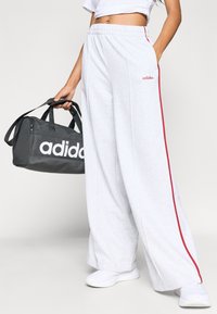 Γκρι φαρδιά φούτερ παντελόνια με κόκκινη πλαϊνή ρίγα και κεντημένο λογότυπο, σε συνδυασμό με γκρι αθλητική τσάντα με εξέχον λευκό λογότυπο.