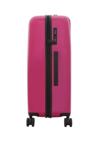 Hard-shell suitcase in bright pink with a black zipper, combination lock, and textured side grip. Four dual wheels for easy maneuverability.