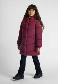 Bordo puffer jakna s kapuljačom, sa štepanim dizajnom i bočnim džepovima. Nosena preko tamnih hlača i crnih cipela.