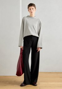 Top de mangas longas listrado em cinza e branco, calças largas pretas e bolsa tote de couro bordô; tecido suave com ajustamento solto e ombros caídos.