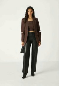 Brown cropped blazer and matching top with cutout sleeves, paired with high-waisted black faux leather trousers and black heels.