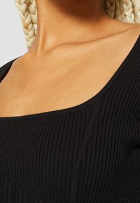 Black ribbed top with a wide neckline, featuring a textured fabric and visible stitching details. Close-up of shoulder area.