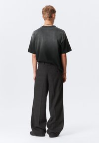 Črna zbledela kratka majica s kratkimi rokavi, v kombinaciji z ohlapnimi sivi karirastimi hlačami, ki prikazujejo sproščen kroj in mehak tekstilni občutek.