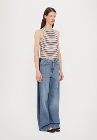 Striped tank top in brown and white, paired with wide-leg light blue jeans. The outfit features casual style and relaxed fit.