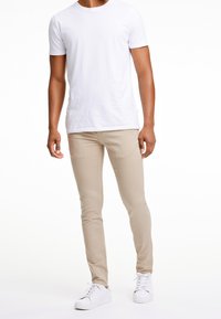 Biała bawełniana koszulka, beżowe slim-fit spodnie i białe sneakersy. Spodnie mają gładką teksturę, podczas gdy koszulka ma klasyczny dekolt w serek.
