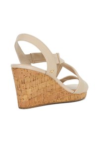 Beige wedge sandalen met een kurken hak, voorzien van een kruisriemontwerp en een verstelbare enkelband. Inclusief gouden hardware accenten.