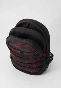 Sac à dos en nylon noir avec plusieurs compartiments zippés et des détails en ligne rouge. Poches intérieures en maille et bretelles réglables pour le confort.