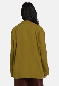 Veste oversize vert olive au design simple, dotée d'un col, de manches longues et d'un tissu légèrement texturé.