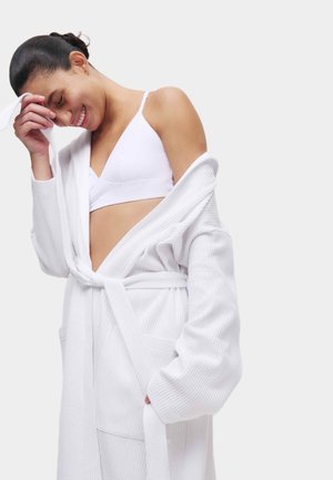 Bata de baño blanca texturizada con mangas largas, envuelta alrededor del cuerpo y atada a la cintura. Cuenta con dos bolsillos frontales y un corte holgado.