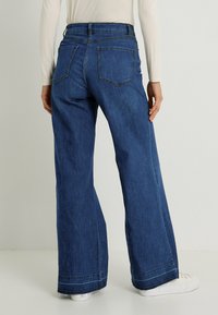 Vaqueros de tiro alto y pierna ancha en denim azul oscuro. Presenta bolsillos traseros, costuras claras y dobladillo sin rematar en la parte inferior.