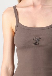 Brun ribbet tanktop med tynne stropper og et lite brodert cowboystøvel- og hattedesign foran. Myk tekstur, tettsittende form.