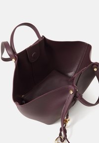Sac en cuir bordeaux avec deux poignées, ouverture sur le dessus, poche intérieure, accents en matériel doré, texture lisse et design structuré.