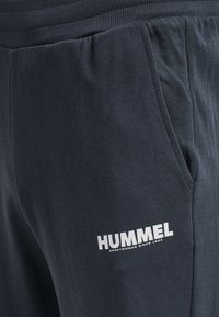 Jūrinės kelnės, pagamintos iš minkštos medžiagos, su elastingu juosmeniu, šoniniais kišenėmis ir baltu „HUMMEL“ logotipu kairiajame šlaunyje.