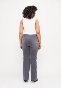 Flared gray pants made of soft fabric, featuring a wide waistband and a smooth texture. Worn with a white sleeveless top.