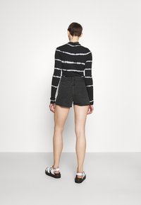 Musta-valkoraidallinen pitkähihaisuus yläosa, joka yhdistetään korkeavyötäröisiin mustiin farkkushortseihin. Mallilla on päällään valkoiset sandaalit, joissa on mustat pohjat.