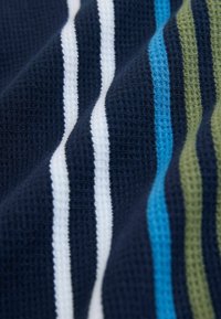 Material tricotat tip vafe de culoare albastru marin, cu dungi verticale în alb, albastru deschis, verde măsliniu și albastru închis, prezentând pliuri și detalii ale texturii.