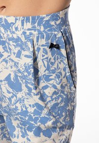Lichtblauwe gebloemde broek met witte bloemenpatronen, voorzien van een zwarte strikaccent bij de zak en een comfortabele tailleband.