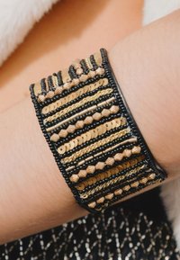 Bracelet en cuir noir et or orné de rangées superposées de paillettes, de perles métalliques et de motifs de travail de perles complexes. Détail de surface texturée.