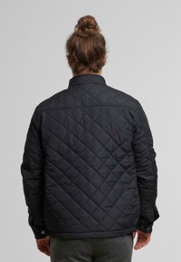 Czarna pikowana kurtka z wysokim kołnierzem, z ukośnymi wzorami stębnowania i zapięciami na napy na mankietach oraz u dołu.