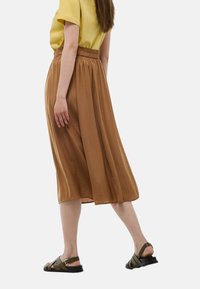 Jupe midi marron avec une coupe ample, taille élastique et texture fluide, associée à un haut court jaune et des sandales noires.