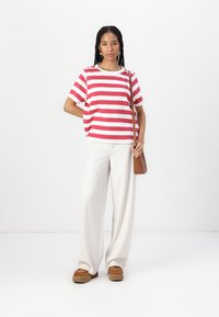 Camiseta de rayas en rojo y blanco, corte relajado, combinada con pantalones anchos blancos y zapatos de plataforma marrones. Pequeño bolso marrón al hombro.