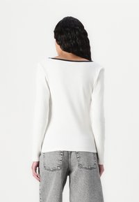 Hvit langermet topp med ribbet tekstur og svart halskant, kombinert med høyt liv grå jeans med sydde lommer.