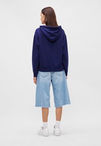 Námornícky modrá mikina s kapucňou, v kombinácii so svetlomodrými džínsovými culottes. Culottes majú rozstrapkaný lem a sú vo voľnom strihu. Na nohách sú biele tenisky.
