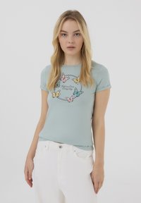 T-shirt aderente azzurro chiaro con maniche corte e scollatura rotonda, decorato con stampe di farfalla colorate e la scritta "Innamorati ogni giorno."