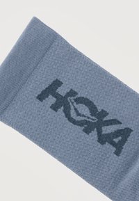 Μπλε πλεκτή κορδέλα κεφαλής με σκούρο μπλε λογότυπο "HKXA" και σχέδιο φύλλου σε λευκό φόντο.