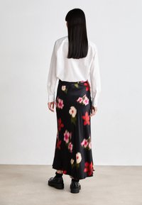 Svart midiskjørt med røde og rosa blomstermønstre, laget av glatt satin. Kombinert med en hvit stripete skjorte med knapper og kraftige svarte sko.