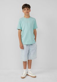 Lichtblauw katoen T-shirt met korte mouwen en een ronde hals, gecombineerd met lichte denim shorts en witte sneakers met een bruine zool.